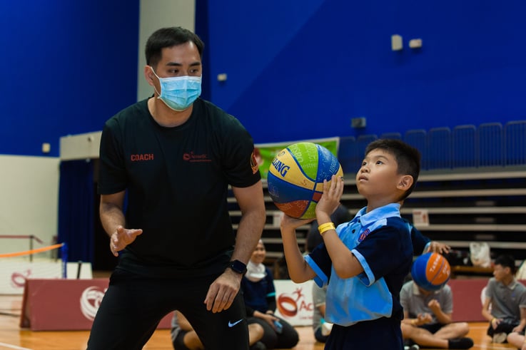 A coach looking on to a boy preparing to throw a basketball into the hoop.