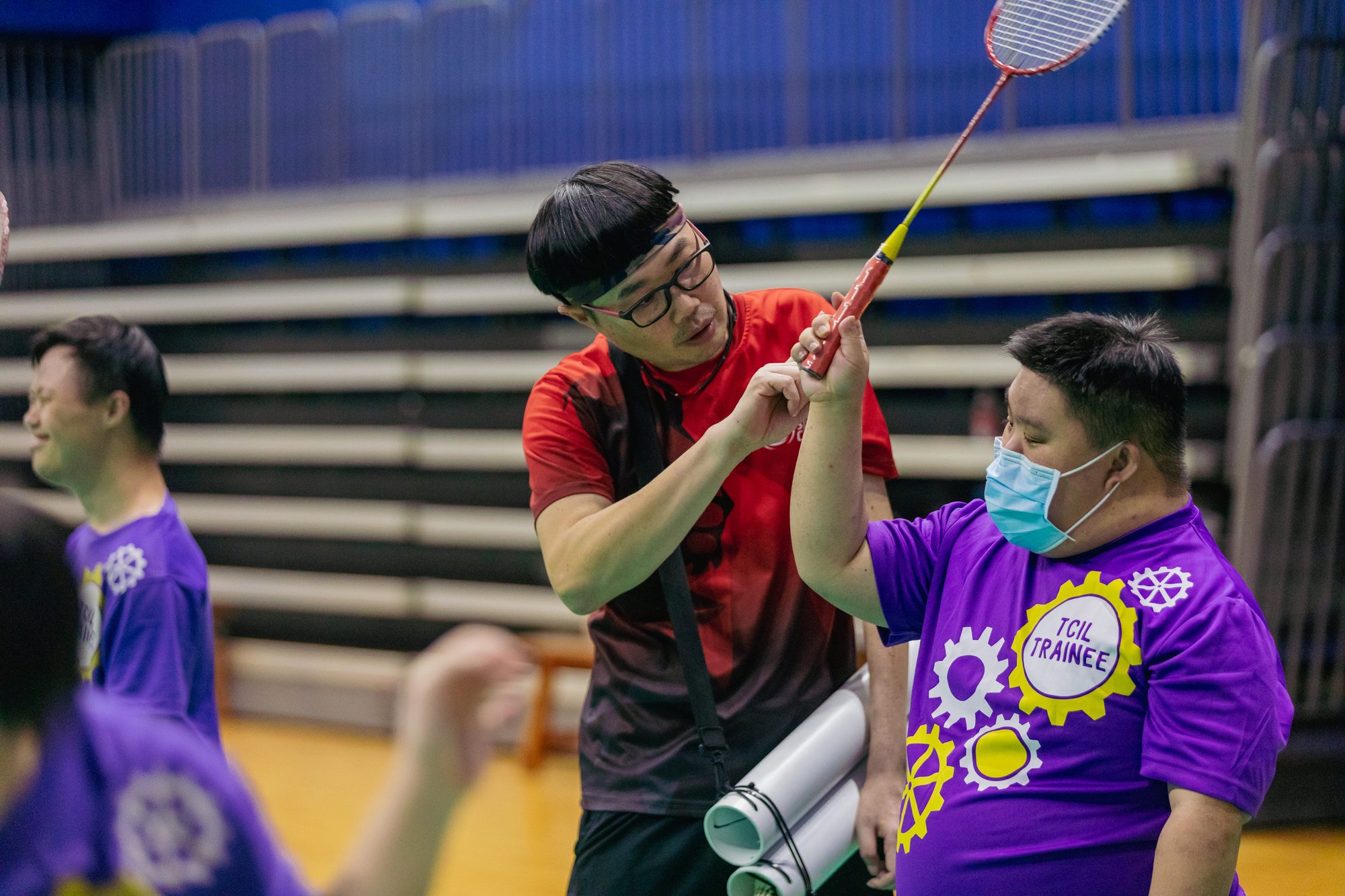 Photo of a badminton coach teaching a player with special needs how to hold a badminton racket slightly overhead