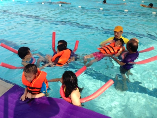 A group of children with special needs using flotation devices in the swimming pool guided by coach and parents