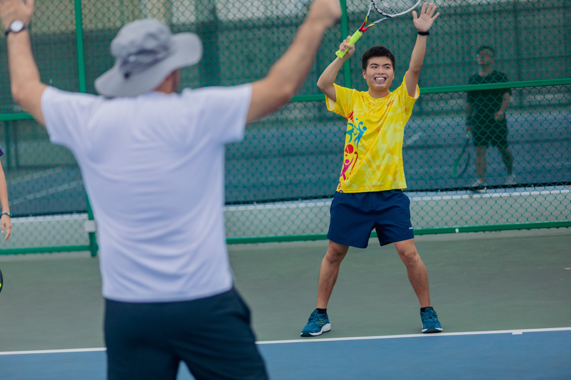 Photo of tennis coach teaching smiling male learner with special needs how to perform an overhead serve