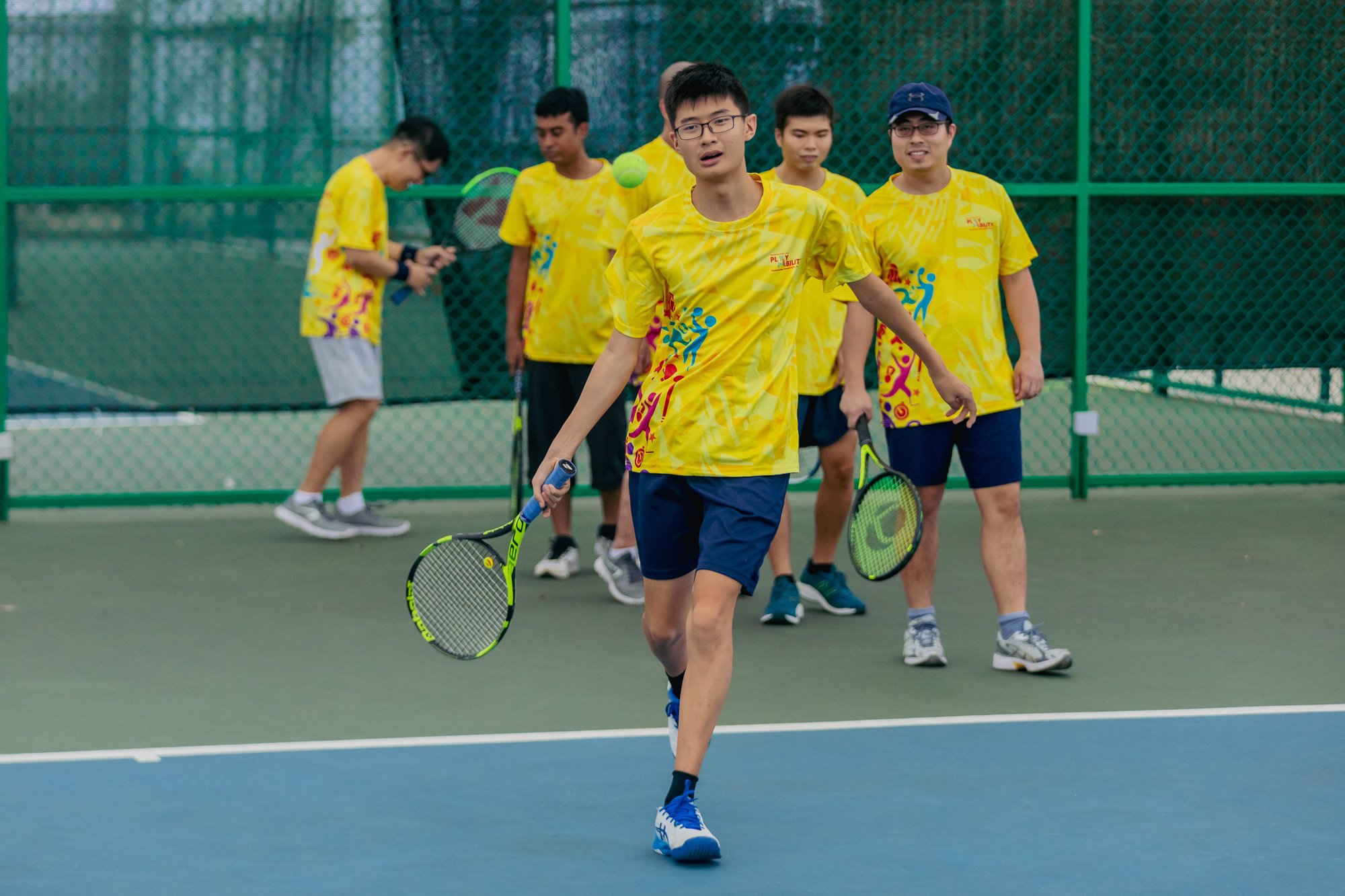 Photo of a group of learners with special needs each holding tennis rackets and taking turns to return a shot