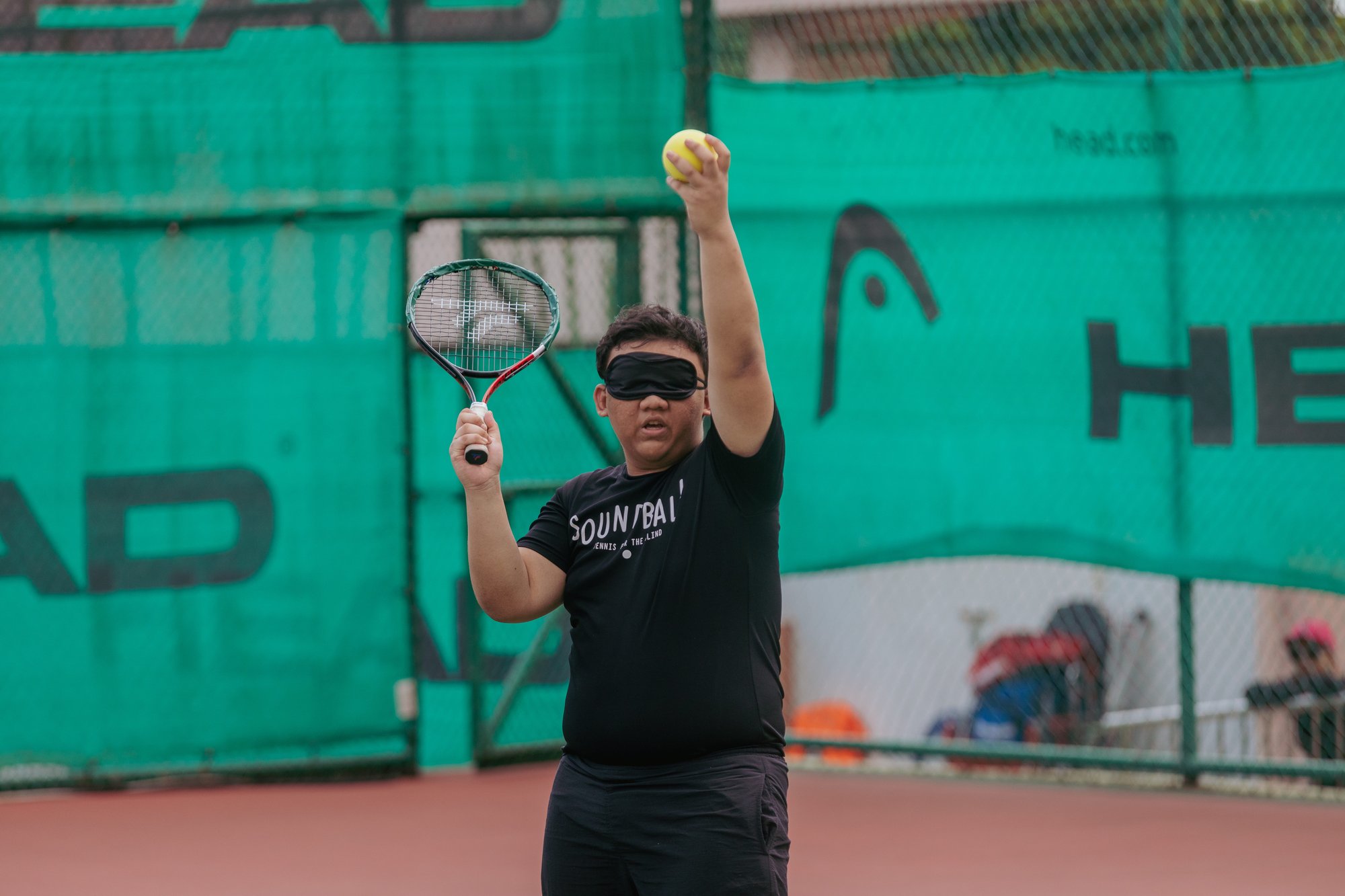 Photo of a male learner wearing eye shades preparing to hit a Soundball ball with a tennis racket